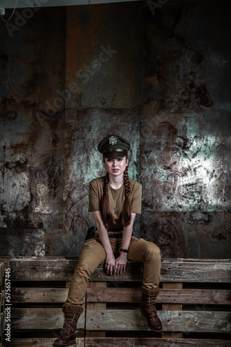 American pilot. A beautiful young woman in a uniform and with a weapon on the background of a metal wall. Staged photo. Studio light. © algrigo