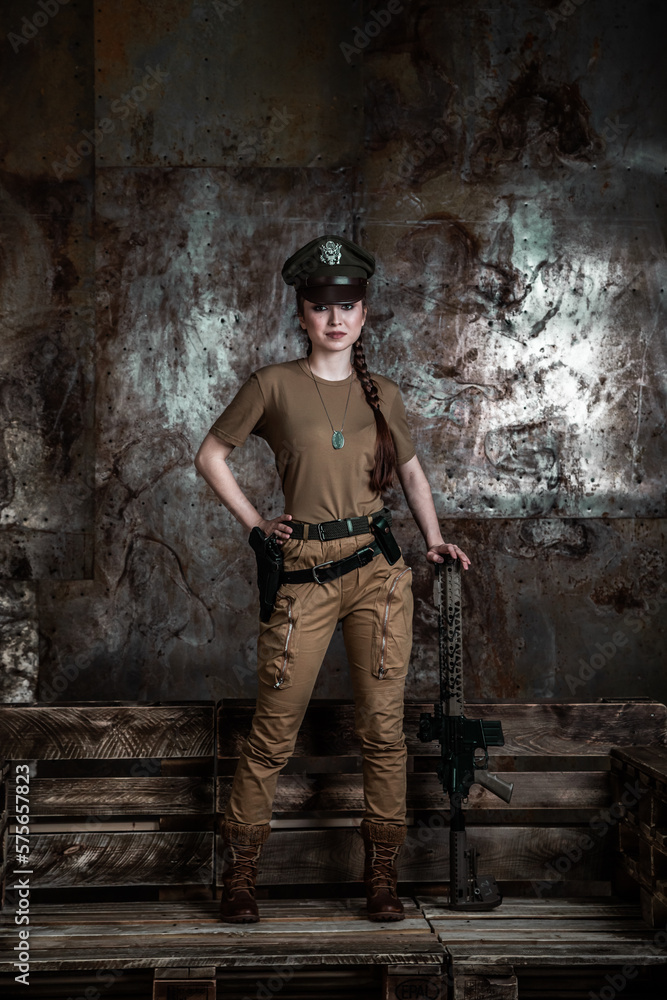 American pilot. A beautiful young woman in a uniform and with a weapon on the background of a metal wall. Staged photo. Studio light. American pilot. A beautiful young woman in a uniform and with a weapon on the background of a metal wall. Staged photo. Studio light.