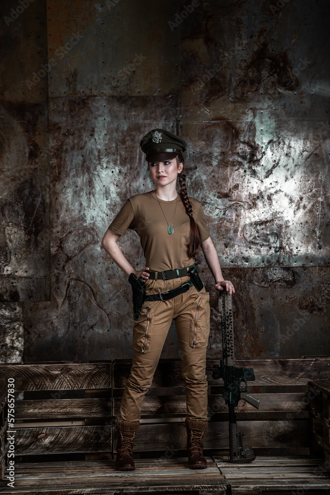 American pilot. A beautiful young woman in a uniform and with a weapon on the background of a metal wall. Staged photo. Studio light. American pilot. A beautiful young woman in a uniform and with a weapon on the background of a metal wall. Staged photo. Studio light.