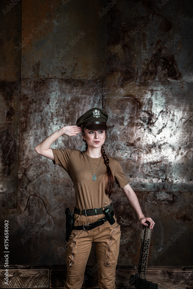 American pilot. A beautiful young woman in a uniform and with a weapon on the background of a metal wall. Staged photo. Studio light.
