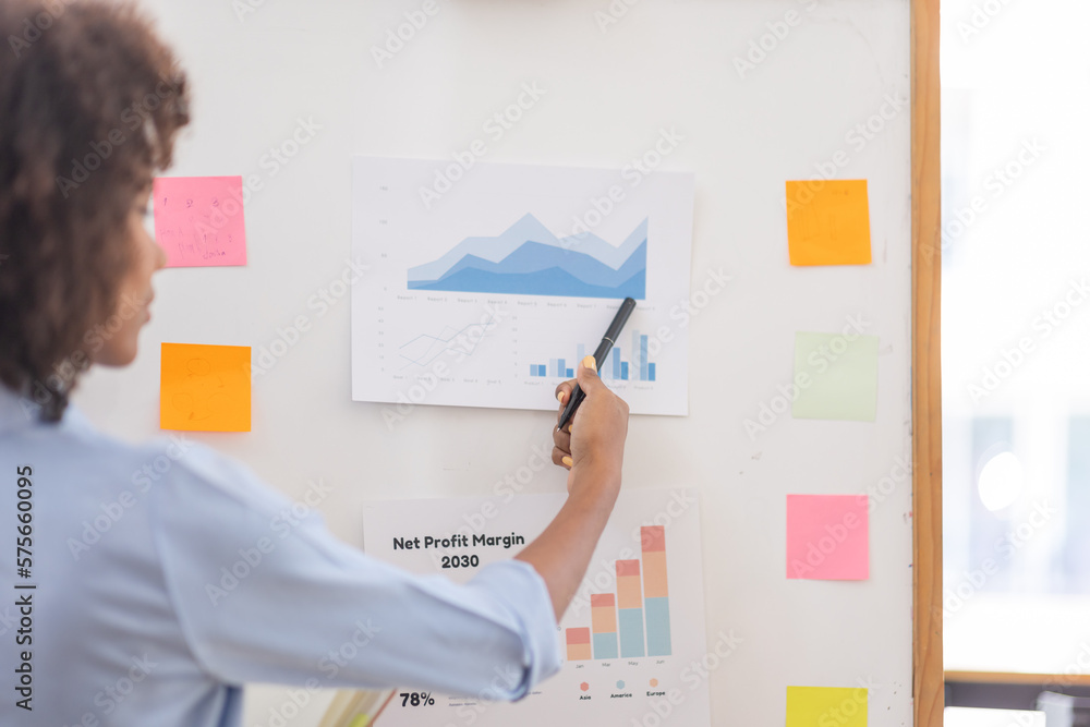 young asian entrepreneur of small company putting a adhesive sticky notes and graph chart on whiteboard in office during analyzing strategy team meeting formulating business strategies. young asian entrepreneur of small company putting a adhesive sticky notes and graph chart on whiteboard in office during analyzing strategy team meeting formulating business strategies.