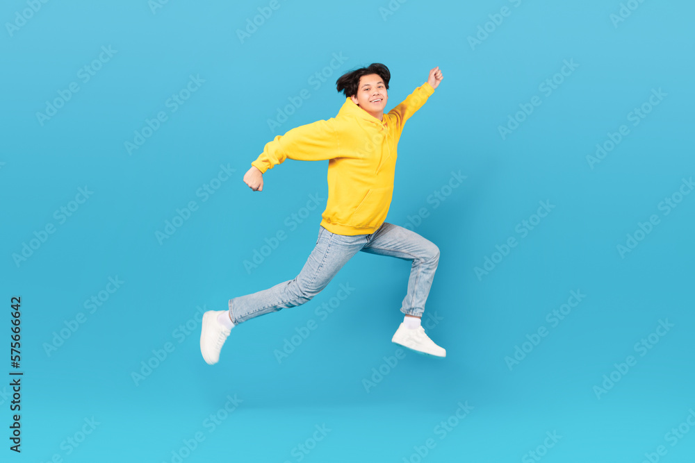 Japanese Teen Boy Jumping In Mid Air Over Blue Background