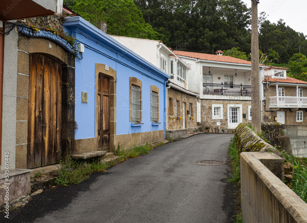 Calle solitaria, asfaltada con casas de color azul y árboles verdes en el pueblo del Ferrol, La Coruña, verano de 2021