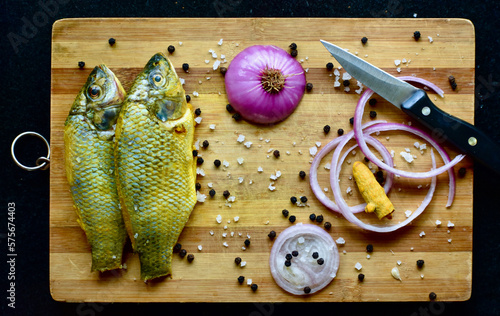 Fresh cut raw river Catla fish, cleaned with turmeric, prepared for baking in the oven with herbs and seasoning on a wooden board.