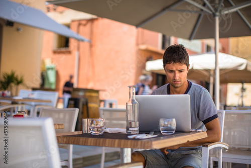 Young male freelancer working on his laptop computer in a city. Confident young business man typing on keyboard outdoors.
