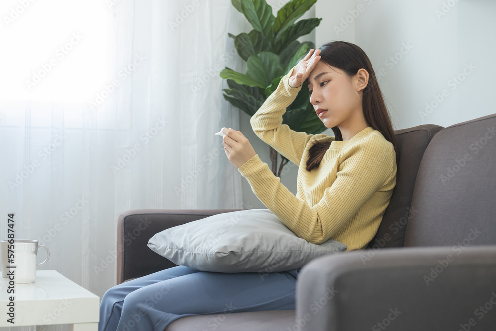 Sick, influenza asian young woman, girl headache have a fever, flu and check thermometer measure body temperature, feel illness sitting on sofa bed at home. Health care person on virus, covid-19. Sick, influenza asian young woman, girl headache have a fever, flu and check thermometer measure body temperature, feel illness sitting on sofa bed at home. Health care person on virus, covid-19.