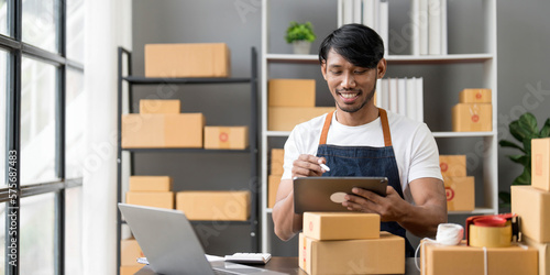 Male online store small business owner entrepreneur seller packing shipping ecommerce box checking website retail order using laptop preparing delivery parcel on table. Dropshipping concept. Closeup © wichayada