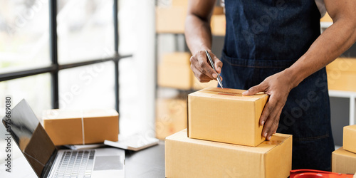 Male online store small business owner entrepreneur seller packing shipping ecommerce box checking website retail order using laptop preparing delivery parcel on table. Dropshipping concept. Closeup