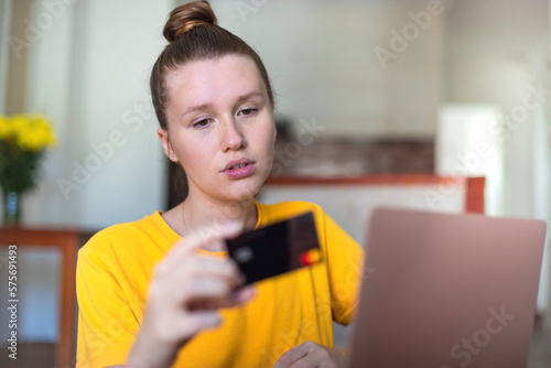 Serious woman entering information from credit bank card on laptop at home, online shopping