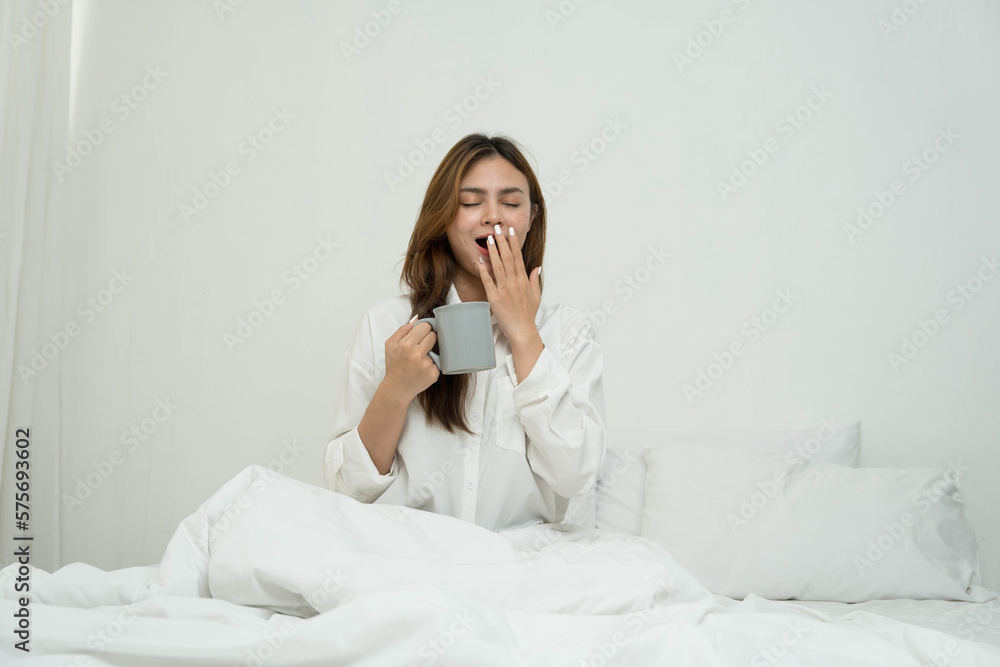 Asian women sitting on bed in the morning after waking up. Young girl on bed in sunny bedroom. Smiling young girl enjoying warm coffee in sunny bedroom. Female drinking coffee on bed in morning. Asian women sitting on bed in the morning after waking up. Young girl on bed in sunny bedroom. Smiling young girl enjoying warm coffee in sunny bedroom. Female drinking coffee on bed in morning.