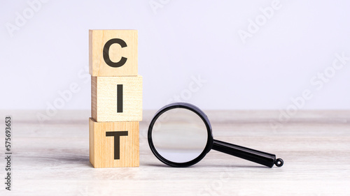 CIT - corporate income tax - text wooden cube blocks and magnifying glass on table. strategy, marketing, and content concept