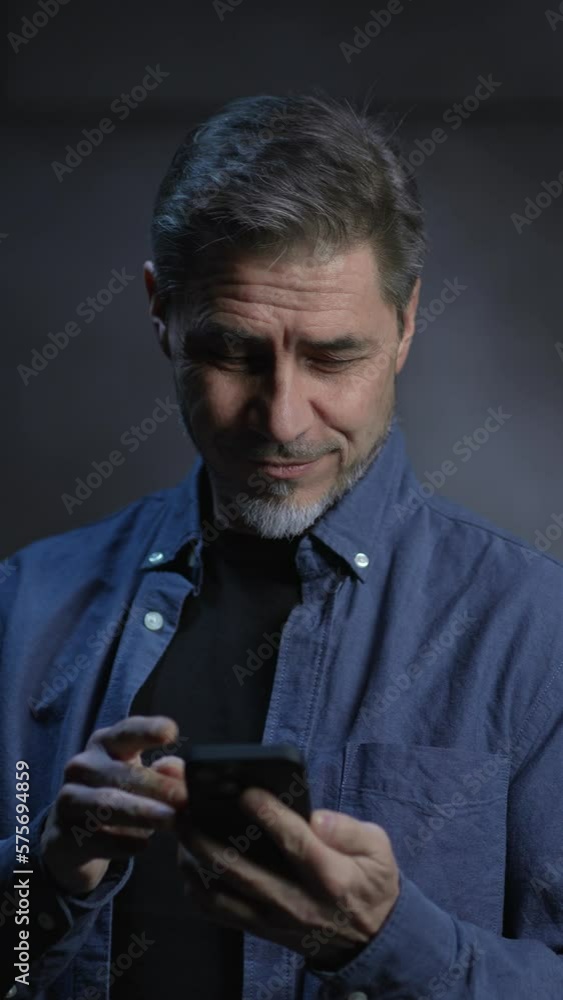 Portrait of happy mature man using phone, smiling, standing in front of dark loft wall. Older, middle aged, mid adult, man in his 40s or 50s in casual shirt. Portrait of happy mature man using phone, smiling, standing in front of dark loft wall. Older, middle aged, mid adult, man in his 40s or 50s in casual shirt.