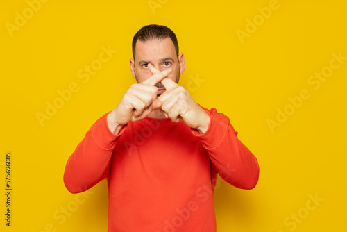 Hispanic man with beard over yellow background expression of rejection crossing his fingers making a rejection sign, he is angry with the ineffectiveness of the authorities regarding climate change. photo