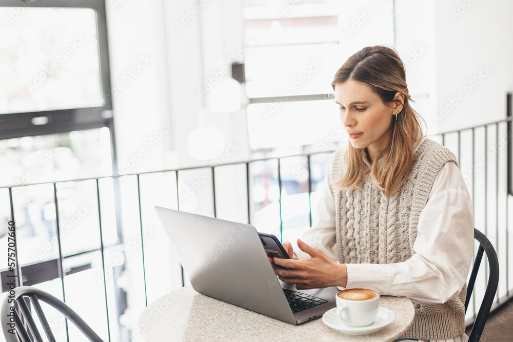 Woman holding smartphone and using laptop on table and coffee in cafe on windows background. Girl using smart phone for business, online shopping, transfer money, financial, internet banking. Woman holding smartphone and using laptop on table and coffee in cafe on windows background. Girl using smart phone for business, online shopping, transfer money, financial, internet banking.