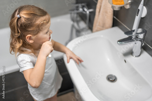 Happy toddler girl brushing teeth in the bath