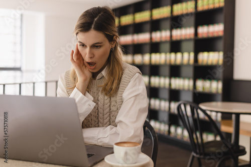 Focused young businesswoman or student looking at laptop. Serious woman working on laptop, look surprised and shock, open mouth. Girl sitting in cafe with cup of coffee.