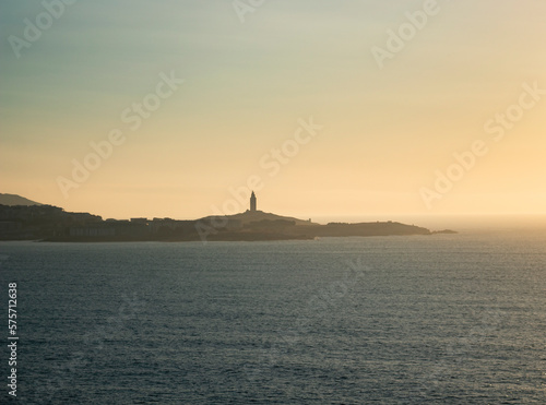 Tower of Hercules on the horizon  illuminated by the last rays of sunlight at sunset. Located in A Coru  a  Galicia  and of historical interest  copy space.