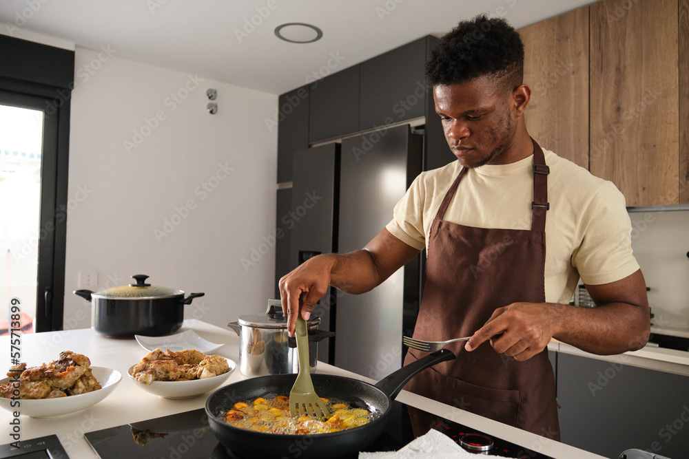 Young black man frying plantains slices in a kitchen.