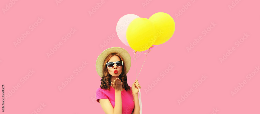 Young woman with colorful balloons blowing her red lips sending sweet air kiss wearing summer straw hat on pink background Young woman with colorful balloons blowing her red lips sending sweet air kiss wearing summer straw hat on pink background
