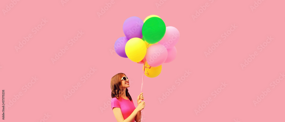 Summer colorful image of happy smiling young woman looking up with multicolor balloons looking up at copy space on pink background Summer colorful image of happy smiling young woman looking up with multicolor balloons looking up at copy space on pink background