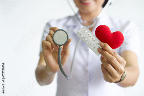 Selective focus on blur stethoscope, pills and red heart in hand of the nurse. Beautiful Asian nurse smile, Medical treatment concept