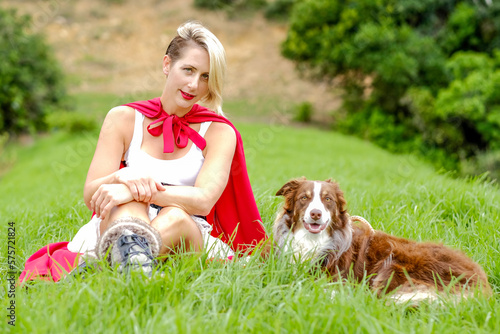 Red Riding hood is sitting in the field with her red wolf a border collie