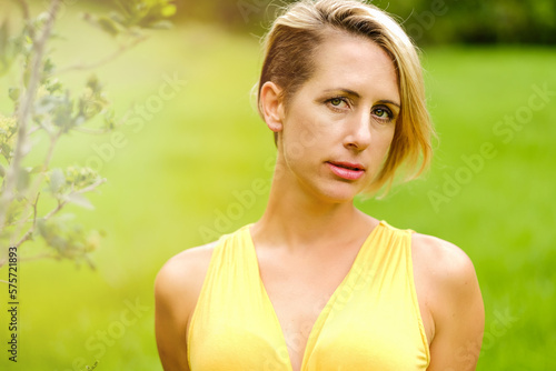portrait of a blonde woman wearing a yellow dress in lime green bushy area