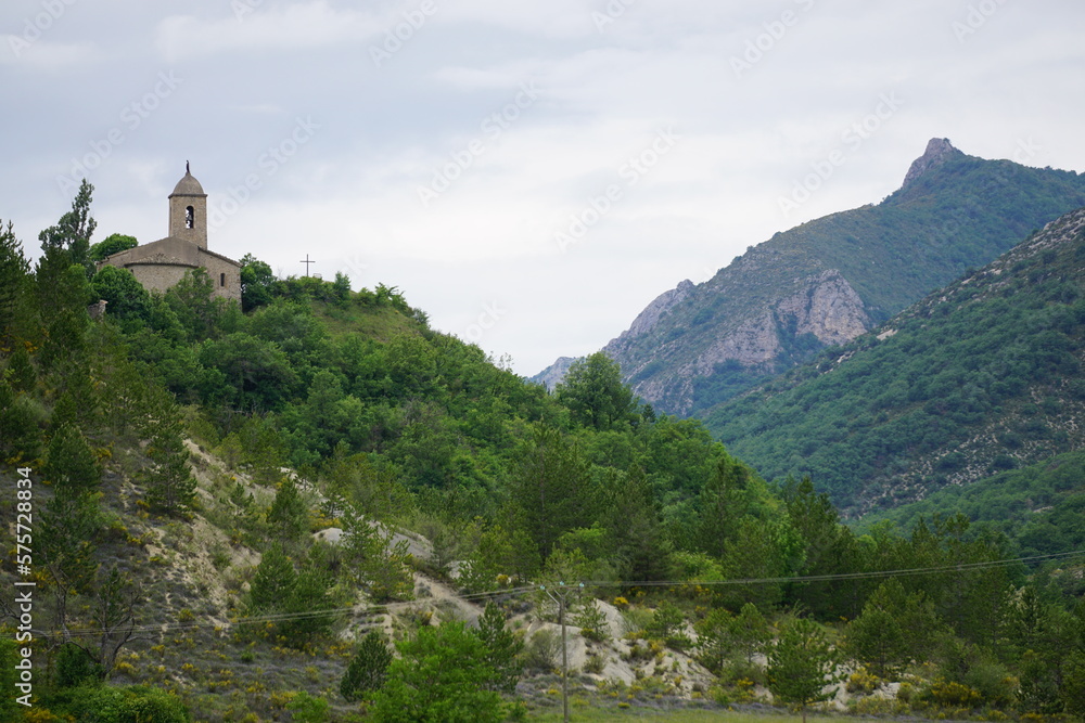 landscape with old stone church on top of the hill of St Vincent sur Jabron and mountains in the south of France