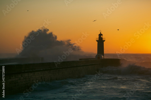 Lighthouse with a huge wave on the Atlantic at dusk, Porto, Portugal.