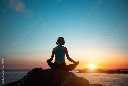 Silhouette of a middle-aged woman doing yoga on the ocean  during sunset.