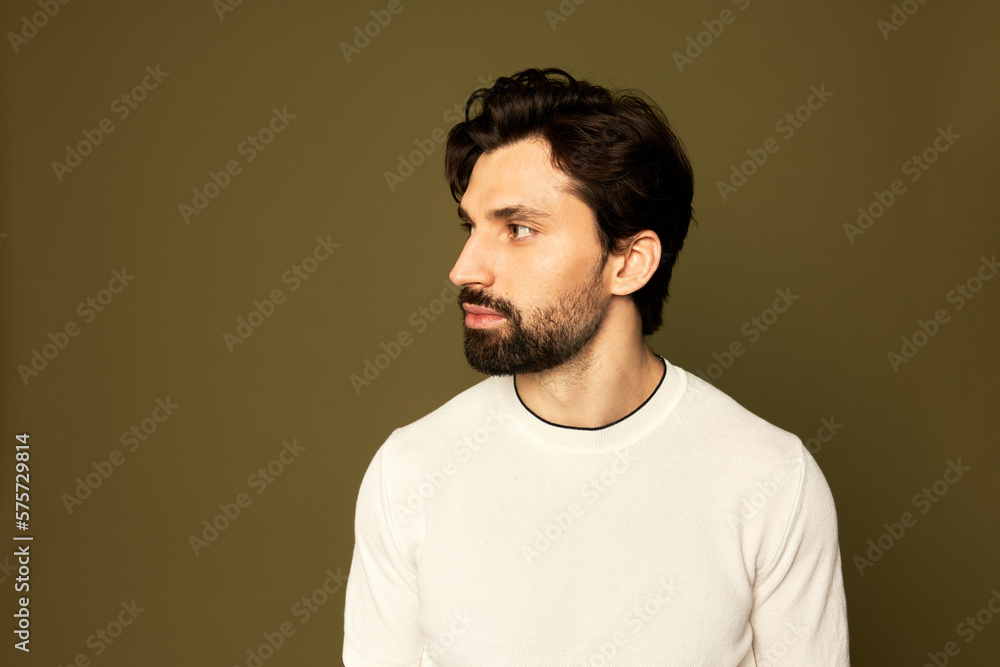 Obraz premium Studio shot of brutal young male fitness instructor of 30s with beard in white mock-up t-shirt looking aside turning head to the right looking at copy space background, isolated on brown