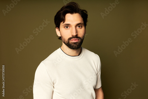 Studio shot of manly photogenic sporty athletic man fitness trainer with stylish haircut and beard, standing against brown background looking at camera with confident serious facial expression © Anatoliy Karlyuk