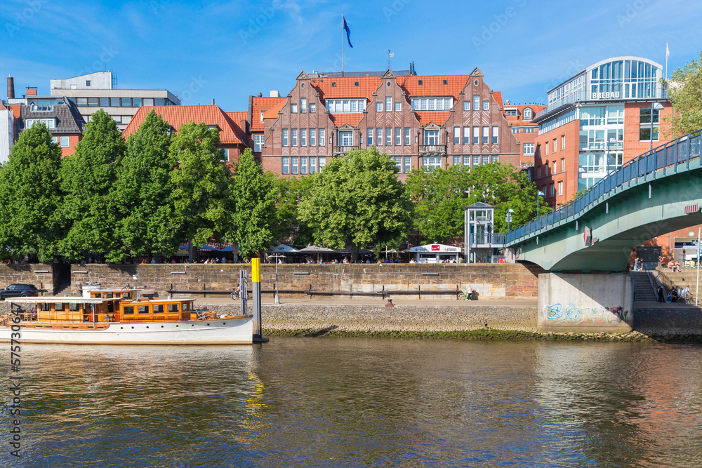 Obraz premium Cityscape of Bremen with old architecture, historical wooden sailing ships and barge floating along the river Weser. Bremen, Germany, July 15, 2021