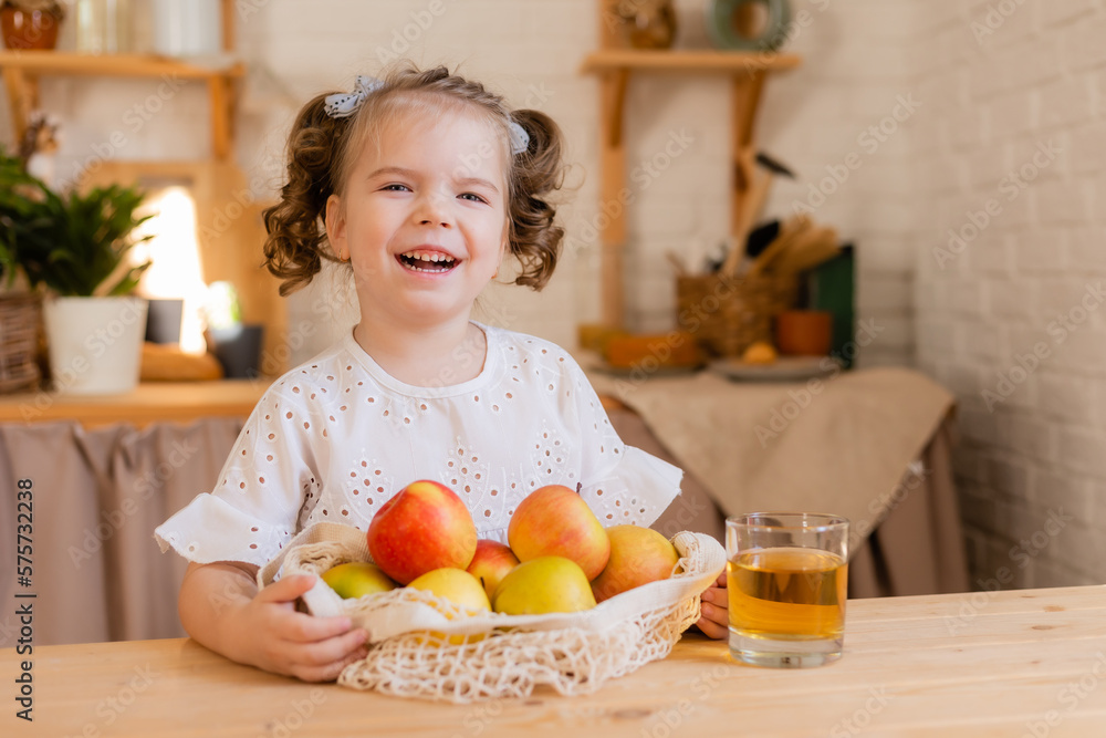 cute little girl in the kitchen at home with apples and a glass of apple juice. Eco-friendly food for children. Space for text