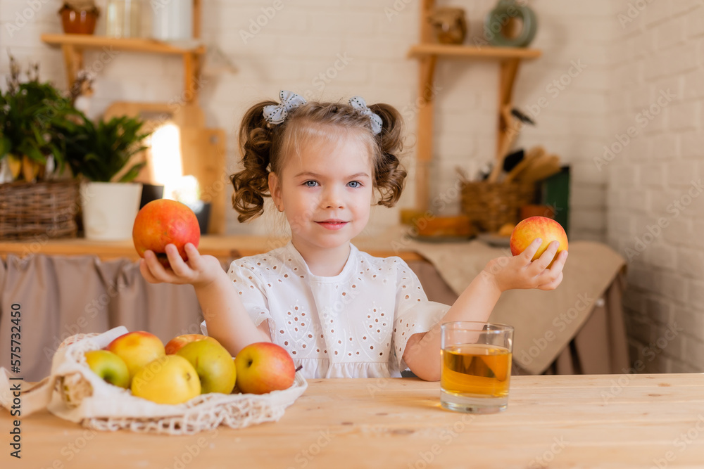 cute little girl in the kitchen at home with apples and a glass of apple juice. Eco-friendly food for children. Space for text