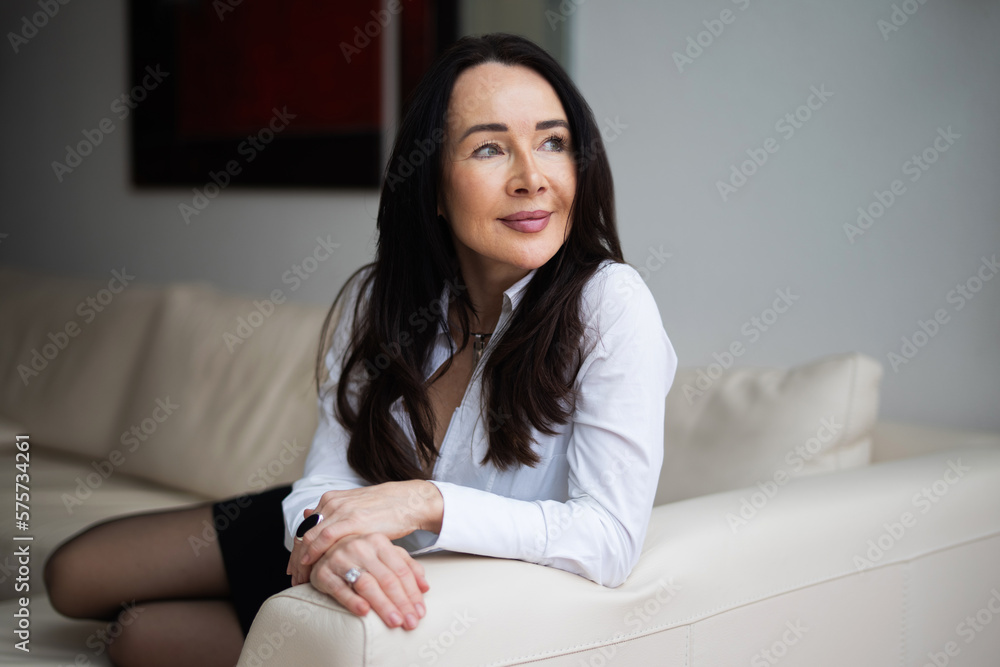 Portrait einer hübschen und attraktiven Frau in weißer Bluse zuhause auf der Couch Portrait einer hübschen und attraktiven Frau in weißer Bluse zuhause auf der Couch