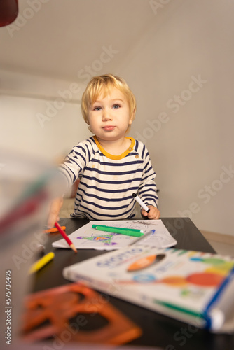Cute little blonde boy drawing with colored pencils