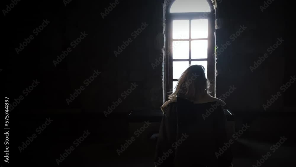 Unrecognizable woman approaching to window with a bright light in dark room Unrecognizable woman approaching to window with a bright light in dark room
