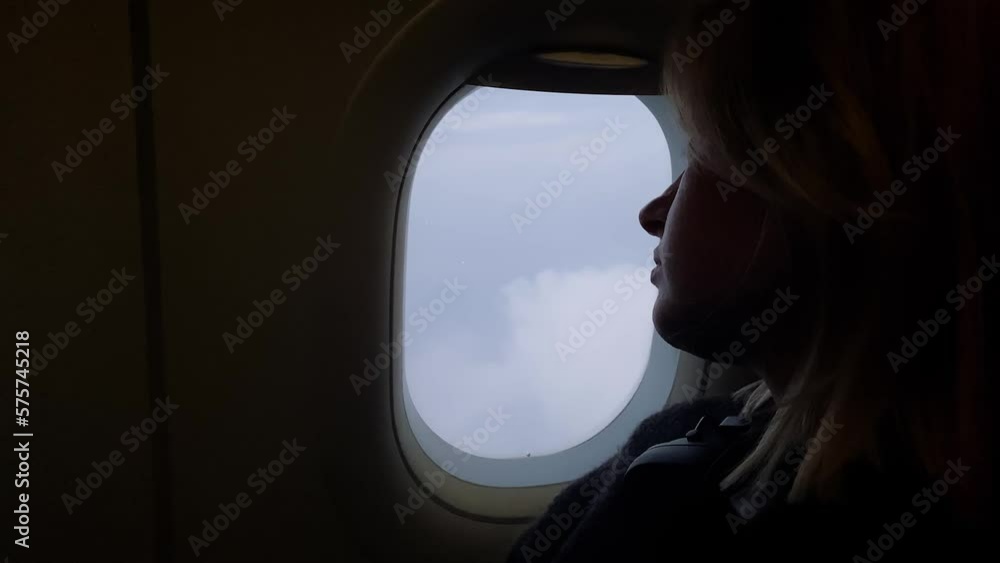 Caucasian blonde woman looking through the airplane window during flight Caucasian blonde woman looking through the airplane window during flight
