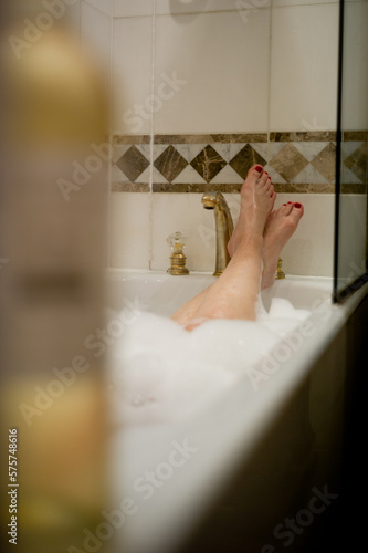 Women feet with red painted toes in a bathtub, with slightly wicked ambience. On the edge of the band bath you can see a cigarette.
