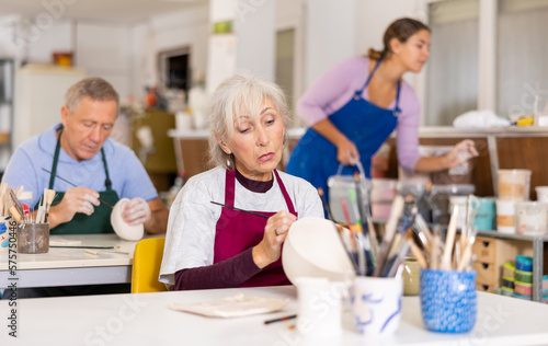 Positive mature woman painting clay ceramic at art studio