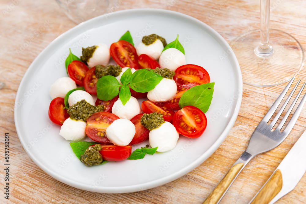 Caprese salad with basil and pesto sauce served on plate. Traditional Italian salad.