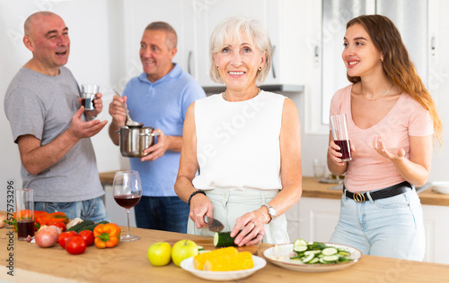 Happy family of four with glasses of wine in their hands is preparing a festive dinner in a home kitchen