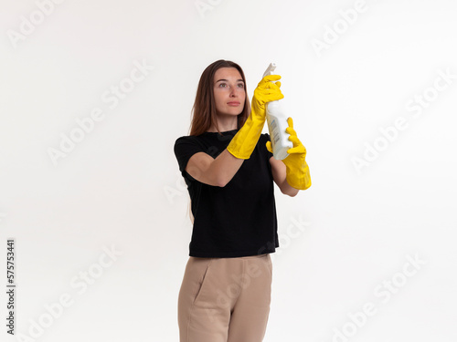 Girl with a sprayer in rubber yellow gloves on a white background. Cleaning of the apartment, office.