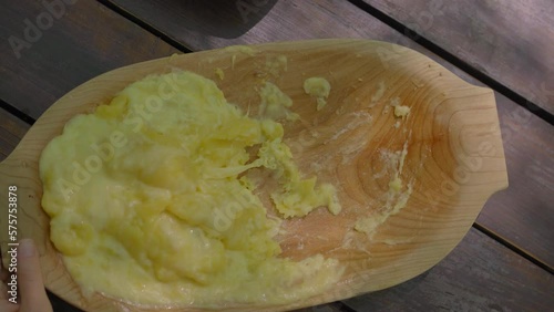 In this stock video, a young woman sits down to enjoy a traditional Montenegrin or Balkan dish known as kajmak or Kacamak served in a wooden bowl. The dish is a creamy blend of cheese, potato and photo