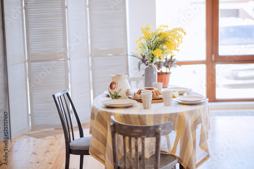 Spring  Easter interior in Scandinavian style. Rustic Living room with a bright wardrobe  yellow mimosa in vase. The table is festively set with ceramic dishes  with a cake on a tray. macrame details