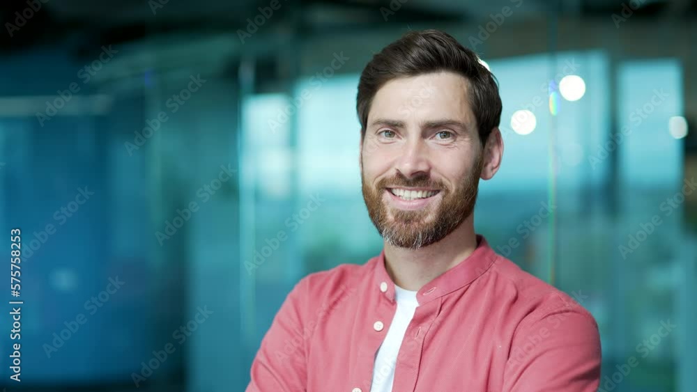 Close up portrait of positive friendly bearded businessman worker looking at the camera at modern glass office workplace Successful attractive smiling entrepreneur freelancer in red shirt indoor alone Close up portrait of positive friendly bearded businessman worker looking at the camera at modern glass office workplace Successful attractive smiling entrepreneur freelancer in red shirt indoor alone