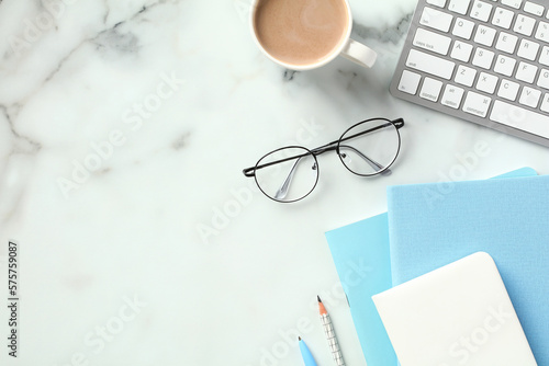 Home office desk table with keyboard, coffee cup, eyeglasses, paper notebooks on marble background. Flat lay, top view. photo