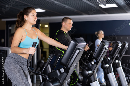 Sporty young woman using elliptical machine in gym