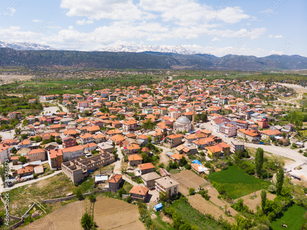 Fototapeta premium Aerial view of typical Turkish small town Yesildag of Burdur province on sunny spring day with snowy mountain range in background..